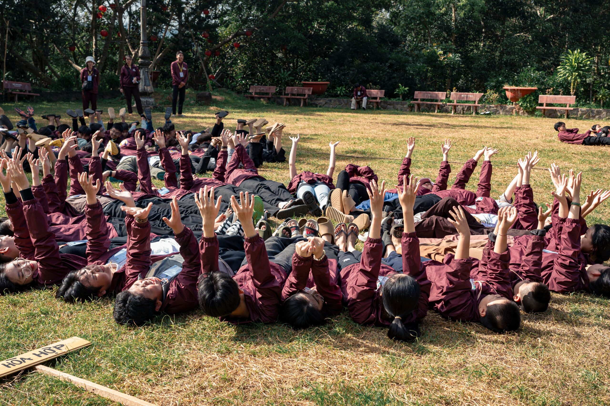 A large group of youth in uniform lying on the grass, raising hands.